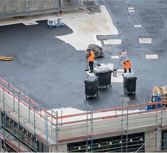 Two contractors in safety gear perform commercial flat roof repair and restoration.
