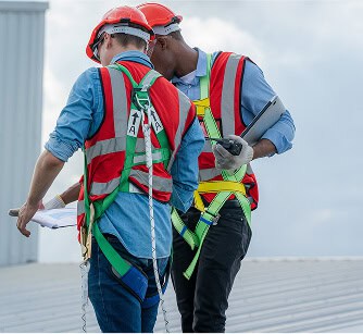 Two roofers inspect a commercial flat roof with plans and tablet for repair work.