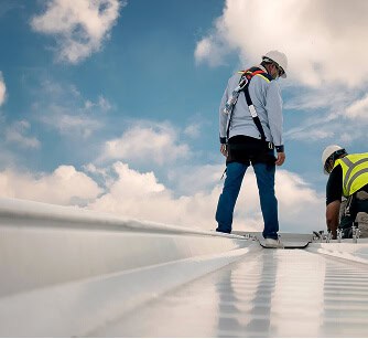 Two workers in safety gear repair a commercial flat roof under cloudy skies.