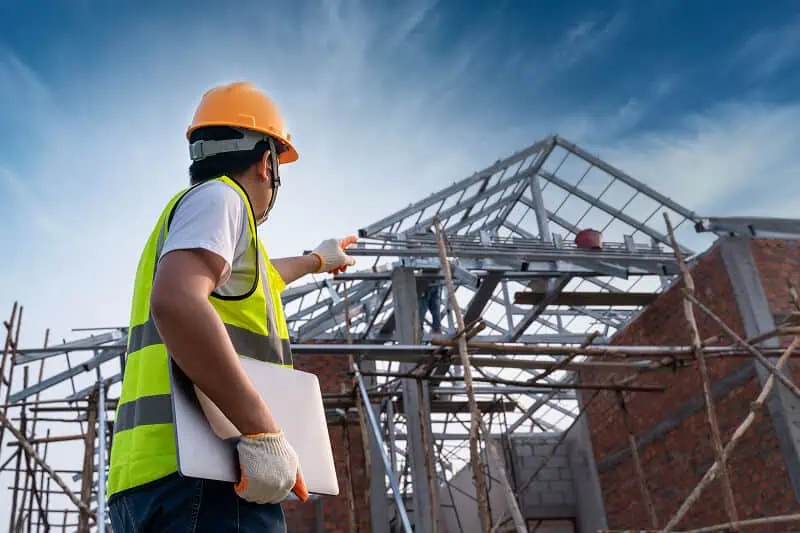 Commercial roofing contractor inspects flat roof restoration on metal building site.