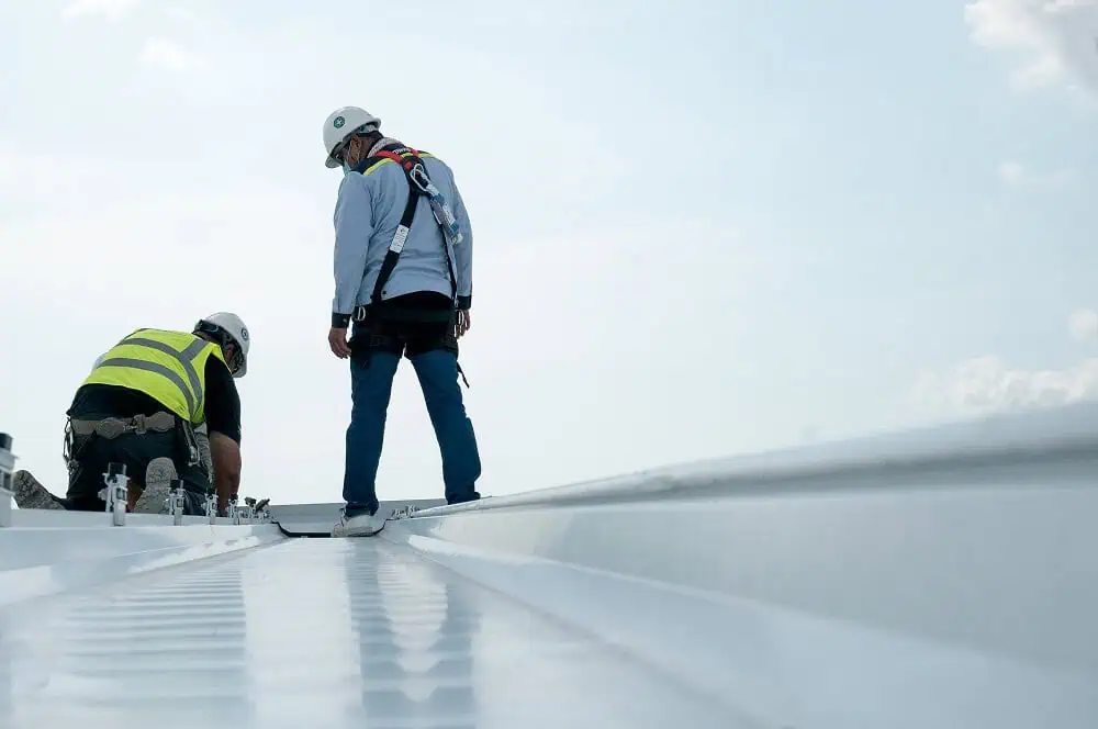 Two workers in safety gear inspect a commercial metal flat roof for restoration.