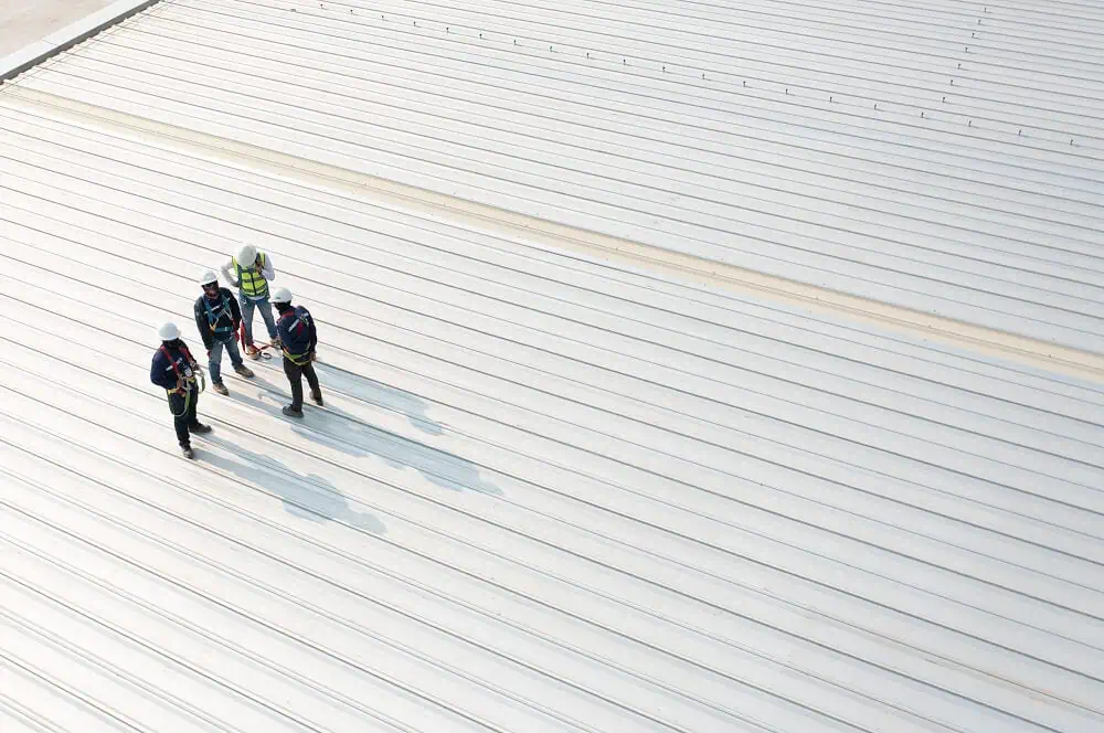 Four roofers discuss commercial flat roof repair and maintenance on a metal rooftop.