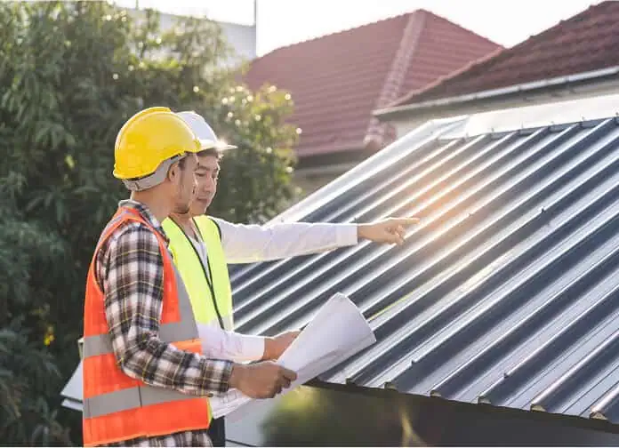 Two workers inspect a commercial flat metal roof for repair and restoration needs.