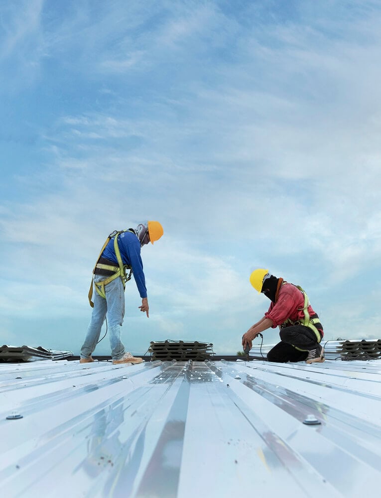 Two roofers in safety gear install metal panels during commercial flat roof repair.