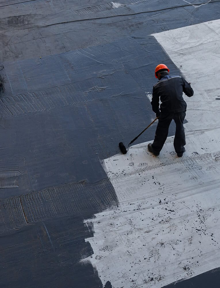 A worker applies coating during commercial flat roof restoration and maintenance.
