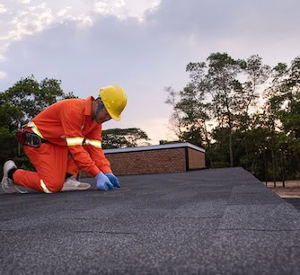 A commercial roofer in safety gear performs flat roof repair at dusk.