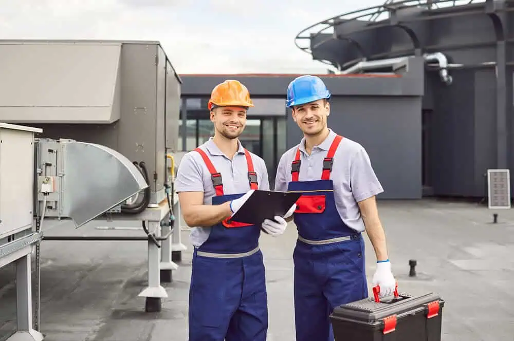 Two workers inspect commercial flat roof HVAC units for repair and replacement.
