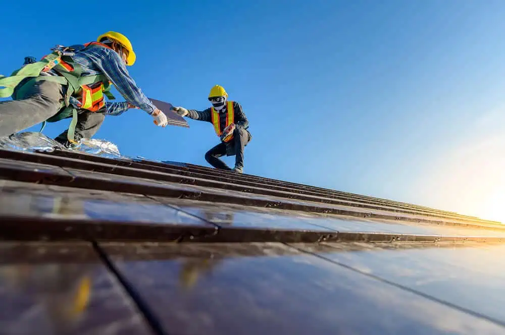Two contractors in safety gear perform commercial flat roof repair and maintenance.