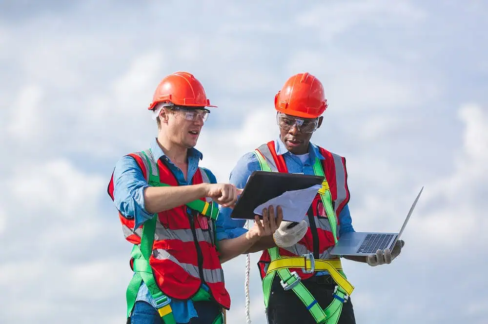 Two workers in safety gear inspect commercial flat roof restoration plans outdoors.