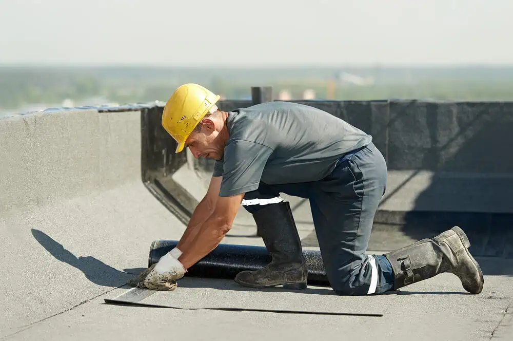 A worker in a yellow hard hat installs flat roofing during commercial roof repair.