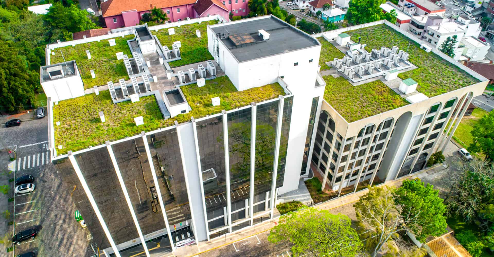 Aerial view of a modern commercial flat roof with green roofing, metal roof, and surrounding trees, illustrating commercial roof repair, flat roof restoration, and maintenance.