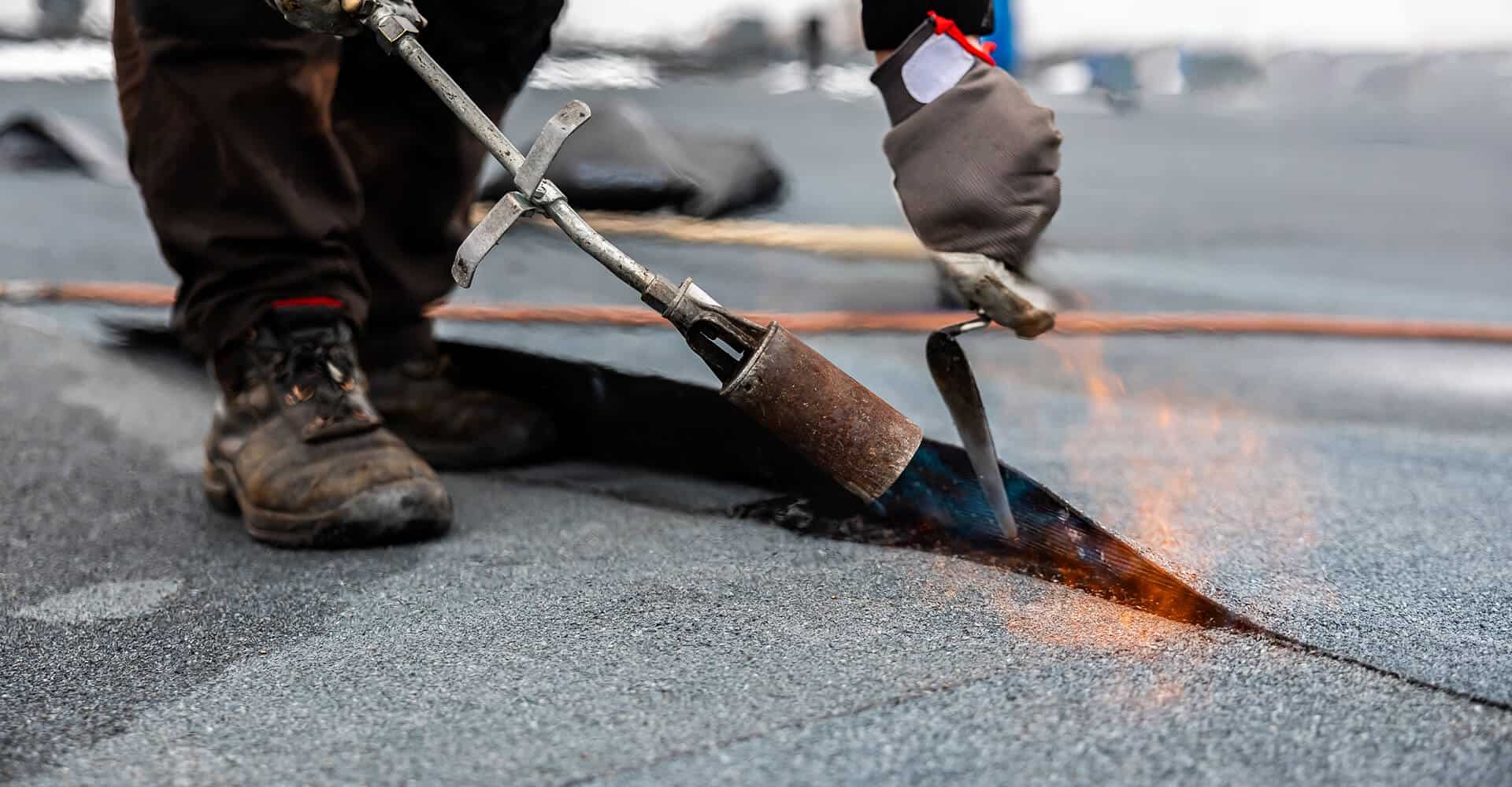 Technician uses torch on modified bitumen for commercial flat roof repair.