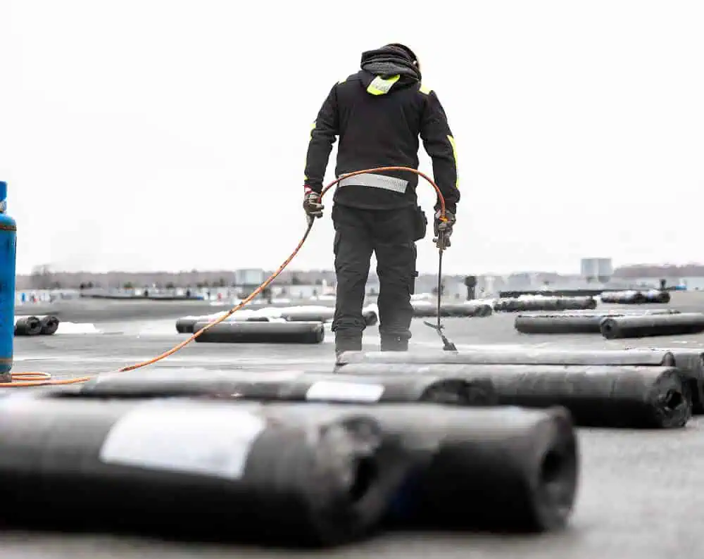 Technician repairs commercial flat roof with torch, showing flat roof restoration.