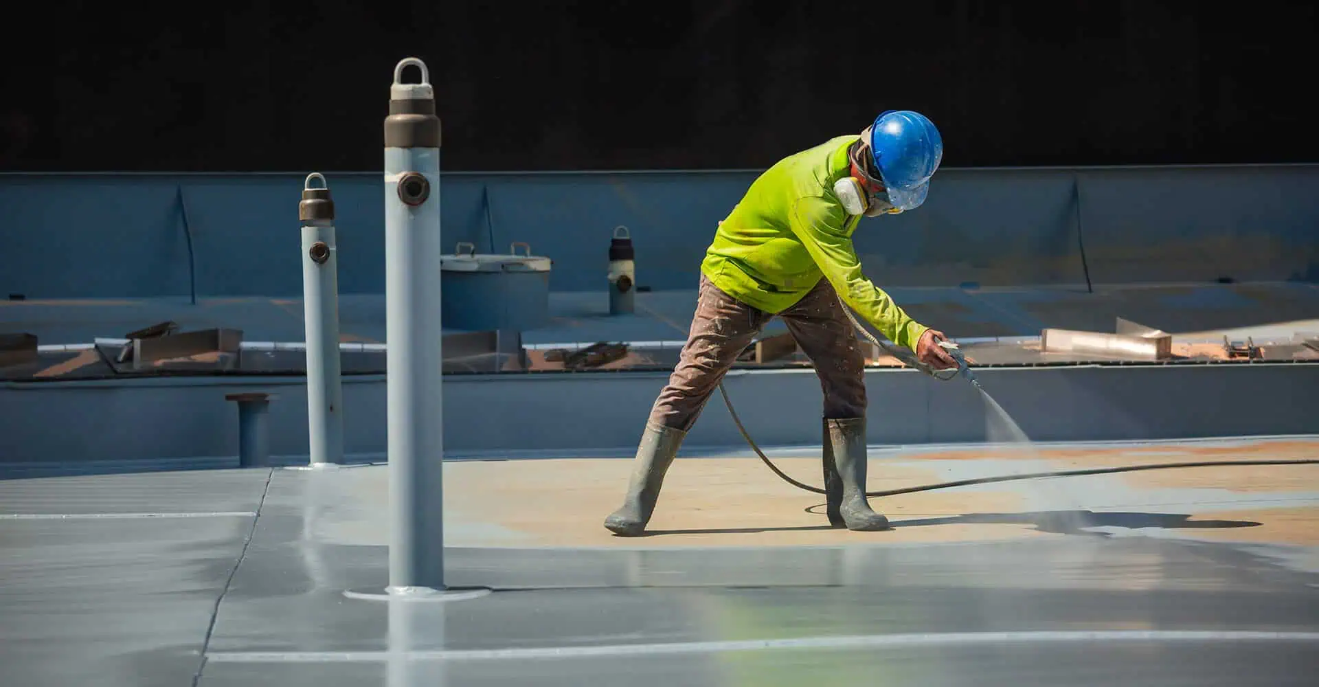 A worker in safety gear applies coating for commercial flat roof restoration.
