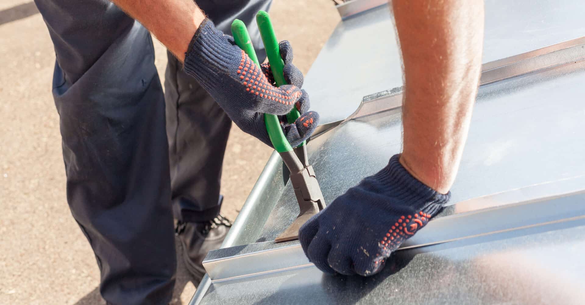 Gloved hands use pliers to bend sheet metal for commercial flat roof repair.