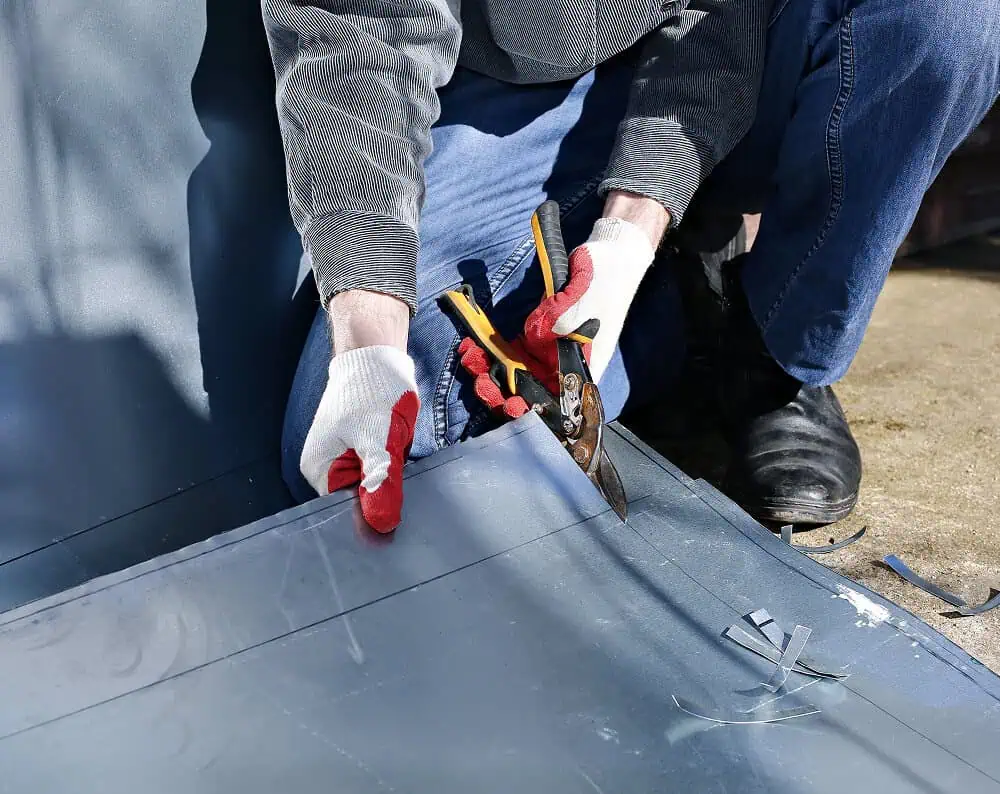 A worker cuts metal with tin snips for commercial flat roof repair and maintenance.