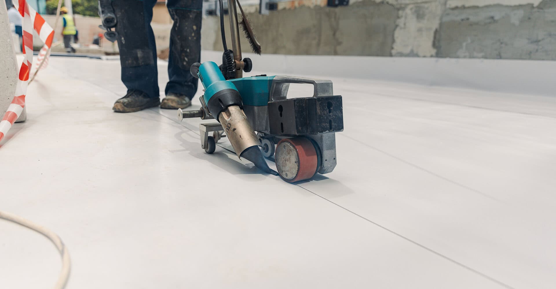 A worker welds a white membrane for commercial flat roof restoration and repair.