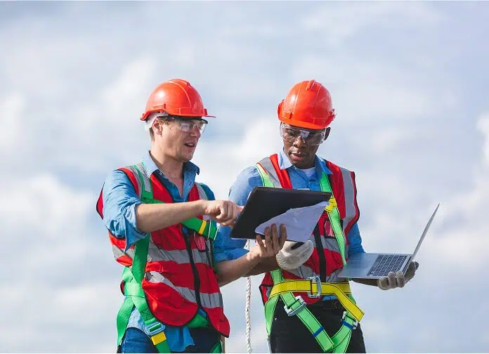 Two workers in safety gear review flat roof restoration plans on a commercial rooftop.