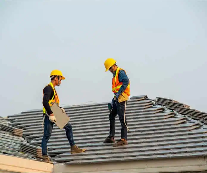 Two workers in safety gear install metal panels for commercial flat roof repair.