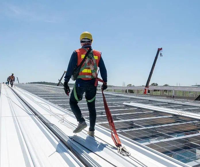 A worker in safety gear walks on a commercial flat metal roof during restoration.