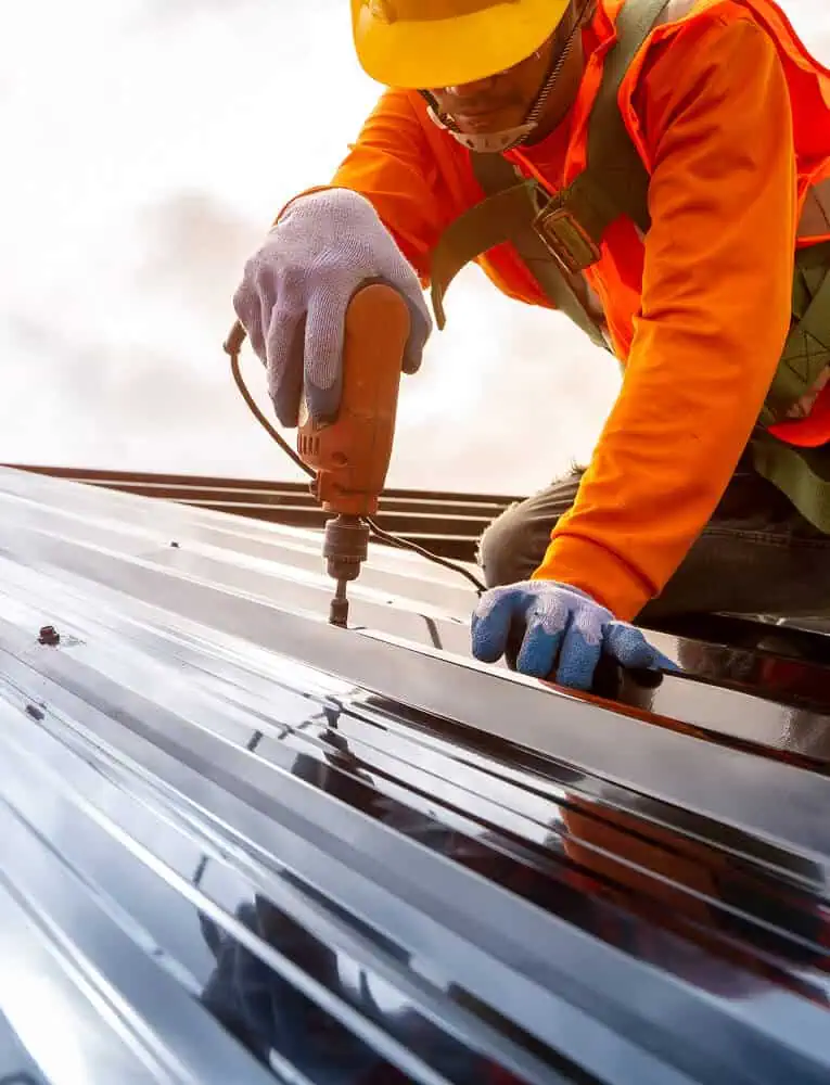 Commercial roofing worker drills metal sheets during flat roof restoration.