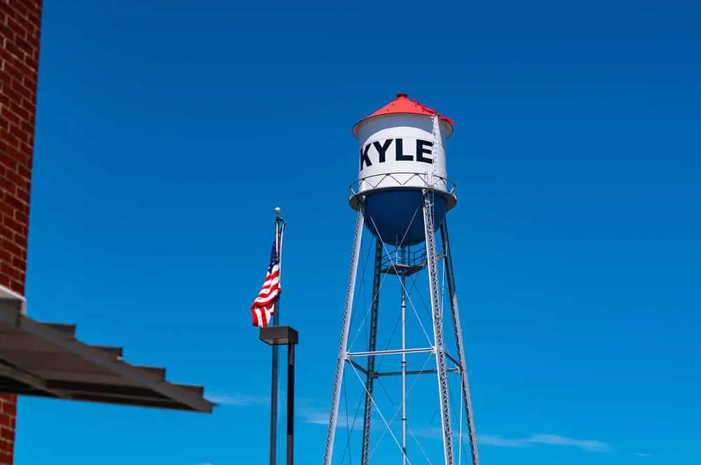 A tall Kyle water tower behind commercial buildings with flat and metal roofs.