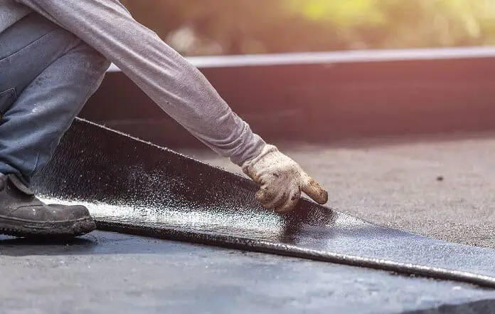A roofer installs black material during commercial flat roof restoration work.