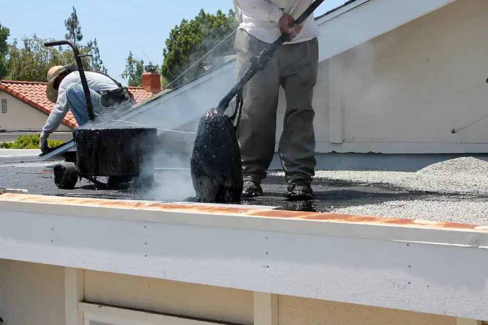 Two roofers embedding gravel in hot tar roof