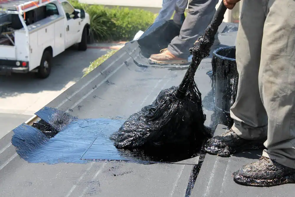 Two roofers applying hot tar roofing material to commercial roof